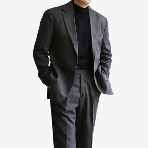 K&ouml;nnte beinhalten: Ein dunkelgrauer Anzug mit einem einreihigen Sakko und einer passenden Hose. Das Sakko hat einen Schalkragen und zwei Pattentaschen. Die Hose hat einen flachen Vorderteil und ein gerades Bein.