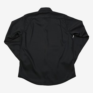 May include: A black long-sleeve shirt with a button-down collar. The shirt is made of a smooth, solid-colored fabric. The back of the shirt is visible, showing the yoke and the curved hemline. The sleeves are long and end in a buttoned cuff.