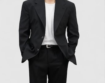 Puede incluir: Un blazer negro con cierre de dos botones, combinado con pantalones negros y una camiseta blanca. El conjunto incluye un cinturón negro con hebilla plateada. El conjunto es de estilo clásico y minimalista.