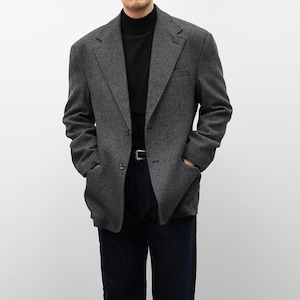 May include: A charcoal gray blazer with a classic two-button closure and notched lapels. The blazer features two front pockets and is worn over a black turtleneck. The person is also wearing dark blue jeans and a silver belt.