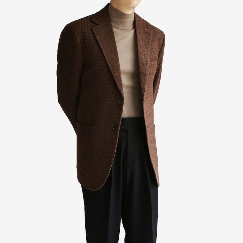 May include: A brown and black plaid blazer with a single button closure. The blazer has a pocket on the left side and is worn over a brown turtleneck sweater.