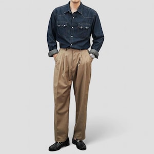 May include: A person wearing a dark blue denim shirt with white stitching and tan pleated trousers. The shirt has two chest pockets and buttoned cuffs. The trousers are paired with black leather loafers.