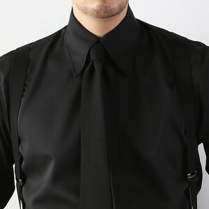 May include: A black dress shirt with a pointed collar and a matching black tie. The shirt is paired with black suspenders. The image is a close-up of the upper body, focusing on the shirt's details and the tie.