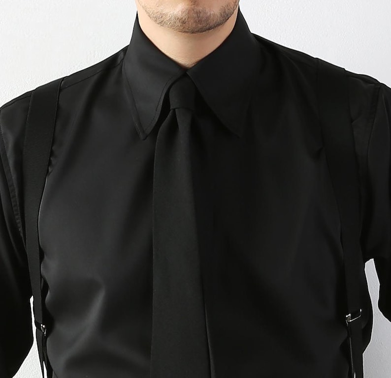 May include: A black dress shirt with a pointed collar and a matching black tie. The shirt is paired with black suspenders. The image is a close-up of the upper body, focusing on the shirt's details and the tie.