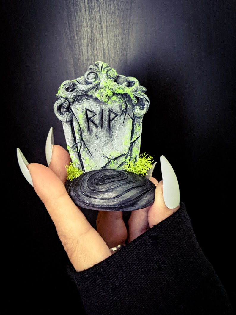 K&ouml;nnte beinhalten: Ein kleiner, grauer und gr&uuml;ner Grabstein mit der Aufschrift "RIP". Der Grabstein steht auf einem schwarzen, spiralf&ouml;rmigen Sockel.