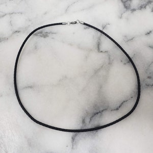 May include: A black leather cord necklace with a silver clasp.