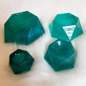 May include: Four teal green geometric resin trinket dishes with a raised center. The dishes are shaped like a diamond with rounded edges.