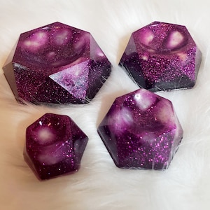 May include: Four purple and white geometric resin dishes with a glittery finish. The dishes are shaped like a multifaceted gem and have a shallow, rounded interior.