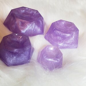 May include: Four purple, iridescent, geometrically shaped dishes with a small indentation in the center. The dishes are made of resin and have a sparkly finish.