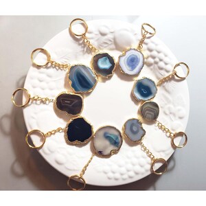 May include: Assortment of agate slice keychains with gold-toned metal rings and chains. Each keychain features a unique pattern of blue, gray, and white agate.