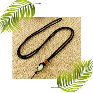May include: A black cord necklace with a white jade pendant. The pendant is tied to the cord with a brown knot.