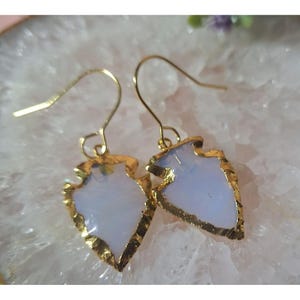 May include: A pair of gold-toned earrings with white arrowhead-shaped stones. The stones have a translucent, milky white color.
