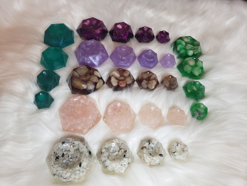 May include: A collection of 20 resin gemstone dishes in various colors and designs, including purple, green, and pink. The dishes are shaped like geometric gems and have different textures, including glitter, pebbles, and sand.