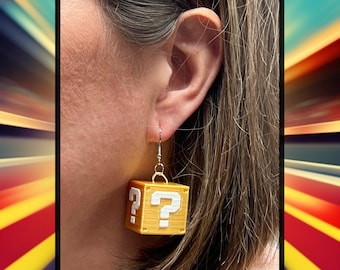 Può includere: Un paio di orecchini a forma di blocco con punto interrogativo dorato. Gli orecchini sono a forma del blocco con punto interrogativo iconico della serie di videogiochi Super Mario Bros.