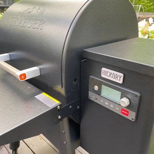 May include: A black Traeger wood pellet grill with a digital control panel and a side-mounted wood pellet hopper labelled "Hickory".