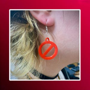 Puede incluir: Un par de pendientes rojos con un símbolo de prohibido. Los pendientes son de plástico y tienen un gancho plateado.