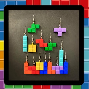 May include: A set of colourful Tetris-shaped earrings. The earrings are made of plastic and are in the shapes of the classic Tetris blocks. The earrings are a fun and unique way to show your love for the classic video game.