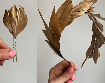 May include: Two gold feather hair clips, one is a single feather and the other is a larger cluster of feathers. The feather clusters are attached to bobby pins.