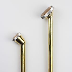 Op de afbeelding: Twee gouden metalen gietstokken met een zilveren spuitmond. De kleinere stok heeft een rode klepknop en de tekst "S.S.A. MADE IN ITALY" gedrukt op de zijkant.