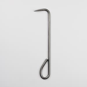 Op de afbeelding: Een zilveren metalen haak met een puntig uiteinde en een lus aan de onderkant.