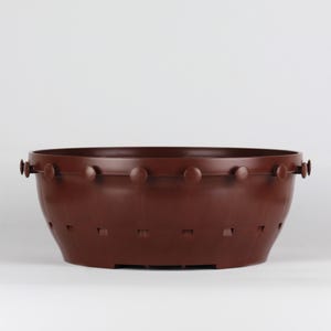 Op de afbeelding: Een bruine plastic plantenbak met een decoratieve rand en een drainagepatroon op de bodem.