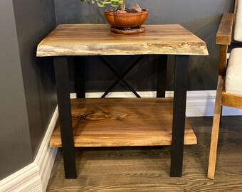 May include: A wooden side table with a live edge top and black metal legs. The table has a shelf and is decorated with a potted succulent plant.