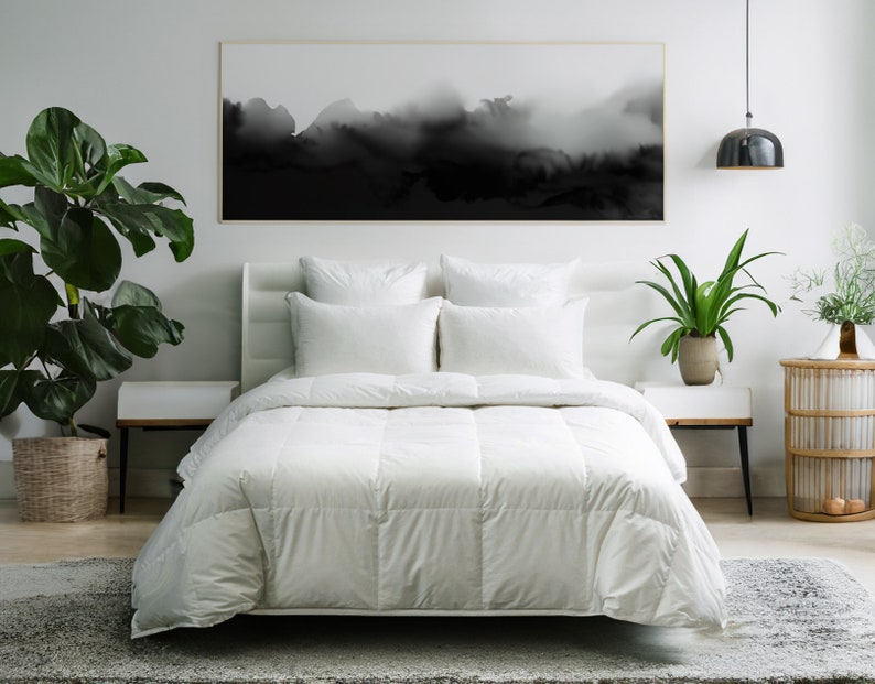 May include: White down comforter on a bed with white bedding and pillows. The bed is in a bedroom with a black and white abstract painting on the wall, a potted plant on a nightstand, and a lamp hanging from the ceiling.