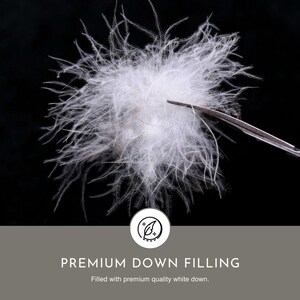May include: Close-up of white down filling, showing the soft and fluffy texture. The down is held by a pair of tweezers against a black background. The text "PREMIUM DOWN FILLING" is displayed below the image, along with the caption "Filled with premium quality white down."