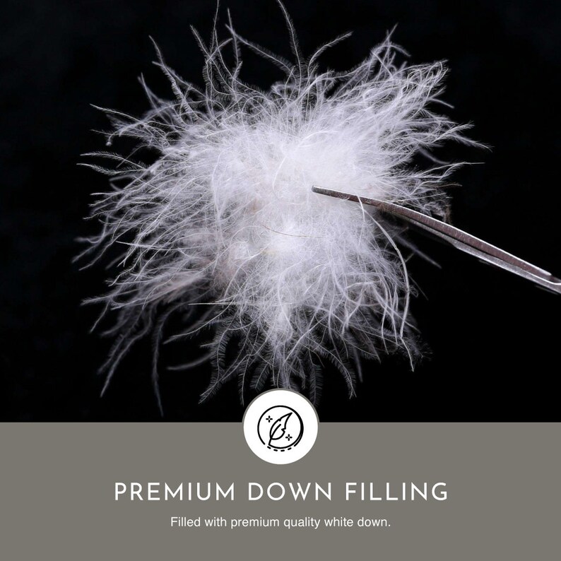 May include: Close-up of white down filling, showing the soft and fluffy texture. The down is held by a pair of tweezers against a black background. The text "PREMIUM DOWN FILLING" is displayed below the image, along with the caption "Filled with premium quality white down."