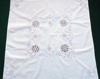 Puede incluir: Mantel blanco con diseño floral bordado en azul y rosa. El diseño presenta delicados círculos de encaje y enredaderas en espiral.