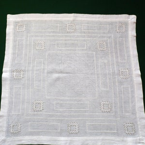 Peut inclure: Nappe carrée en lin blanc avec un motif géométrique brodé délicat. Le motif présente une série de carrés et de rectangles, créant une bordure symétrique et complexe.