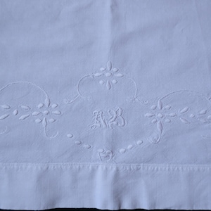 Pode incluir: Tecido de linho branco bordado com um desenho floral e as iniciais "M.B." no centro.