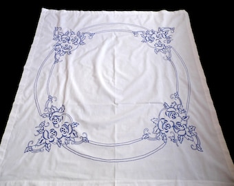 May include: White tablecloth with a blue embroidered floral design. The design features a circular pattern with four floral motifs at the corners.