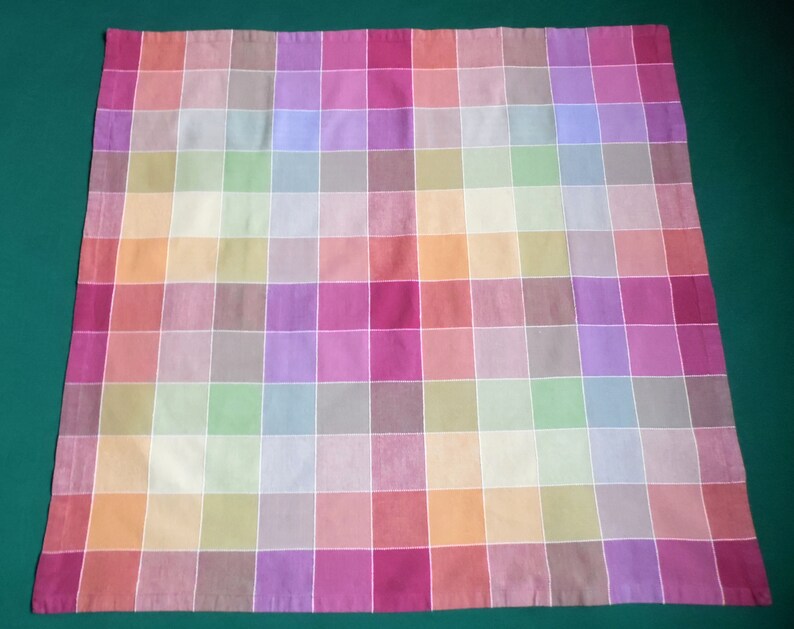 May include: A colorful checkered tablecloth with a variety of pastel colors, including pink, purple, green, and orange.