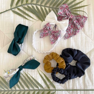 Puede incluir: Surtido de accesorios para el cabello en varios colores y patrones, incluyendo verde, blanco, negro e impresiones florales. Los accesorios incluyen diademas, scrunchies y cintas para el cabello.