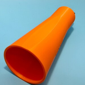 May include: Bright orange, cone-shaped object with a wide opening and a narrower top. The interior is a deep orange, contrasting with the exterior. The object is set against a light blue background.