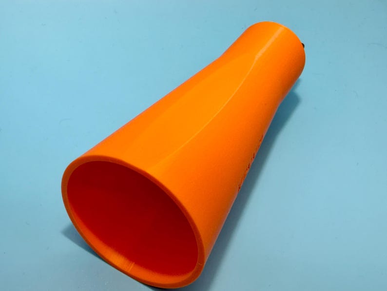 May include: Bright orange, cone-shaped object with a wide opening and a narrower top. The interior is a deep orange, contrasting with the exterior. The object is set against a light blue background.