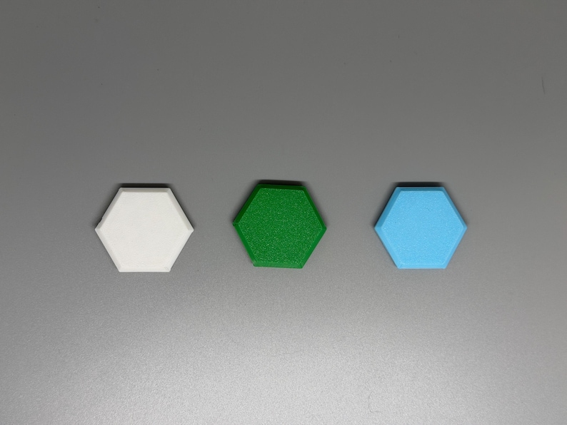 May include: Three hexagonal objects in white, green, and light blue are arranged horizontally against a gray background. The objects appear to be made of a textured material, with the green object having the most visible texture.