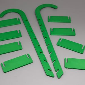 May include: Bright green plant support stakes and matching rectangular clips. The stakes are curved at the top and have notches along the sides. The clips have slots on each end. These items are designed to support plants.