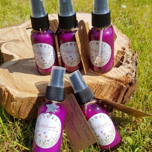 May include: Five small purple glass bottles with spray tops and labels that say "Wildflower Healing". The bottles are arranged on a wooden surface with a brown tag that reads "Made with herbs & essential oils 3 Reiki by Wildflowers www.wildflowershealing.com".
