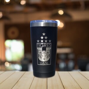 May include: A black stainless steel tumbler with a silver lid. The tumbler has a white engraved logo with the words "TIGRES" and "UANL" and a tiger head graphic.
