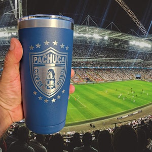 May include: A blue stainless steel tumbler with a silver lid. The tumbler has a silver logo with the text "Pachuca Club de Futbol" and five stars.