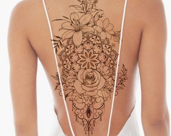 May include: A detailed black and white tattoo design featuring a mandala, a rose, lilies, and other floral elements. The design is intricate and delicate, with a flowing, feminine aesthetic.