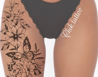May include: Black and white line art tattoo design of a butterfly and flowers on a person's thigh. The tattoo design is on the left thigh and includes a large flower, a butterfly, and smaller flowers.