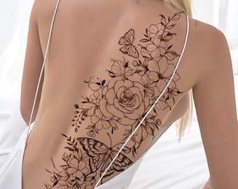 May include: A black line drawing tattoo design of a large rose with leaves and a butterfly on a person's back. The tattoo design is on the right side of the back and extends from the shoulder to the lower back.