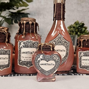 May include: A selection of decorative potion bottles in different sizes. The bottles are reddish-brown with gold accents, including dripping wax-like details. Each bottle features a label with the word "Amortentia".