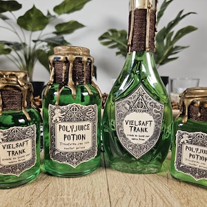 May include: Four green glass potion bottles with gold wax seals and labels. The labels read "VIELSAFT TRANK" and "POLYJUICE POTION". The bottles are different sizes and shapes, with a decorative design.