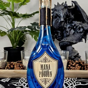 Op de afbeelding: Een blauwe glazen fles met een gouden waszegel en het opschrift "Mana Potion" op een etiket. De fles heeft een decoratief ontwerp en bevat een blauwe vloeistof. Het is een fantasy-item.