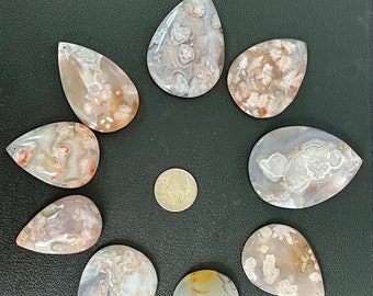 May include: Ten teardrop-shaped agate stones with a variety of brown, white, and gray patterns. The stones are arranged in a circle on a dark gray surface.