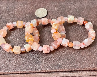 May include: Three pink and orange agate stone bracelets with square beads. The bracelets are stacked on top of each other.
